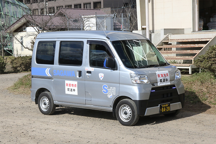 銀色の軽バン。SAGAWAロゴと救援物資輸送中の表示がある。