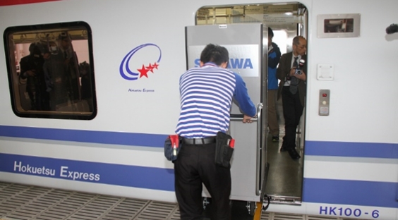 Hokuetsu Expressの白い車両と、開いたドアの前で荷物を運び込む人物、奥に複数の人。