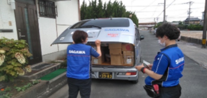 SAGAWAの制服を着た2人。1人がSAGAWA軽ワゴン車の荷台を開け、もう1人が端末を操作している。荷台には段ボール箱。