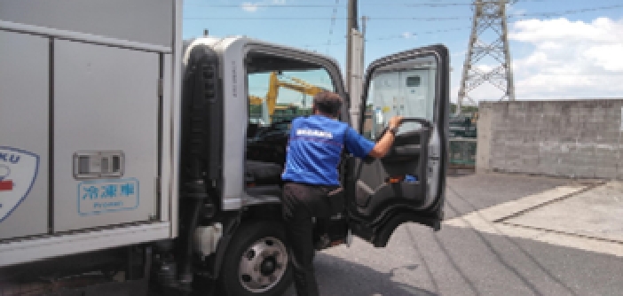 青いシャツを着た人物がトラックの運転席に乗り込む後ろ姿。荷台には冷凍車という文字が記されている。