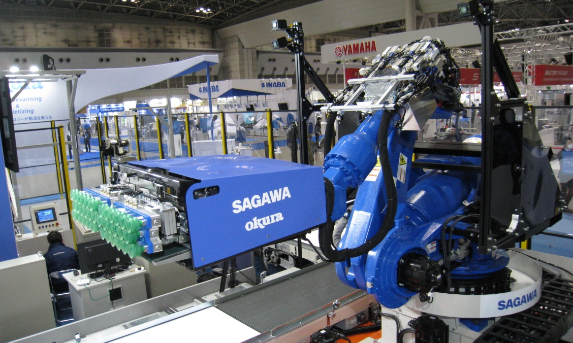 屋内施設に設置された、SAGAWA okuraのロゴが入った青い大型ロボットアーム。周囲にはベルトコンベアがある。