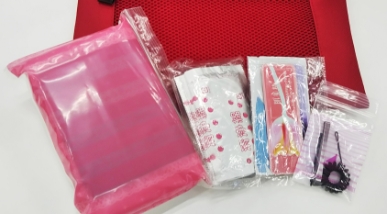 赤いメッシュ素材のポーチの上に並べられた複数のビニール袋。ピンク色の半透明の袋や、ハサミとヘアゴムが入った透明な小袋が置かれている。