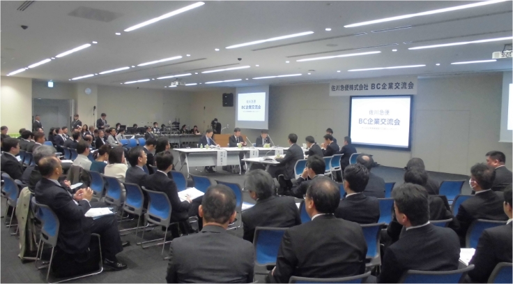 佐川急便株式会社 BC企業交流会会場。多数の参加者が集まり、壇上の登壇者とスクリーンを見ている。