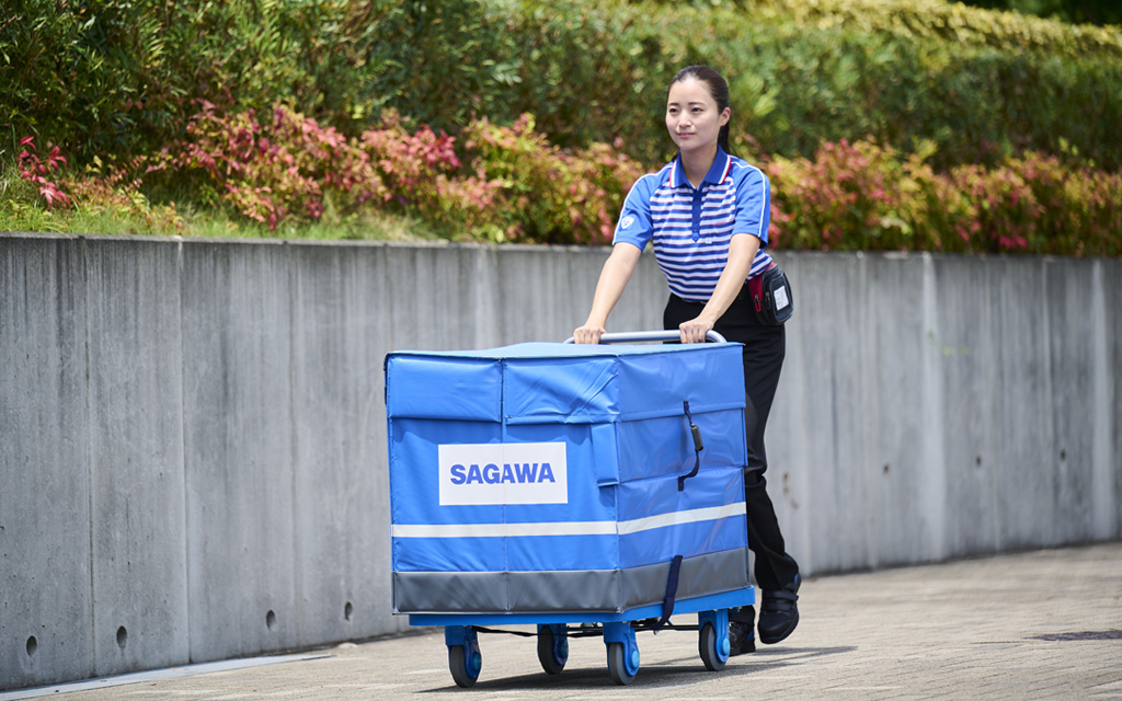 青と白のポロシャツを着た人物が、SAGAWAと書かれた青い台車を押す。