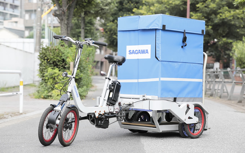白い三輪自転車。フレームと青い箱型の荷台にSAGAWAのロゴ。