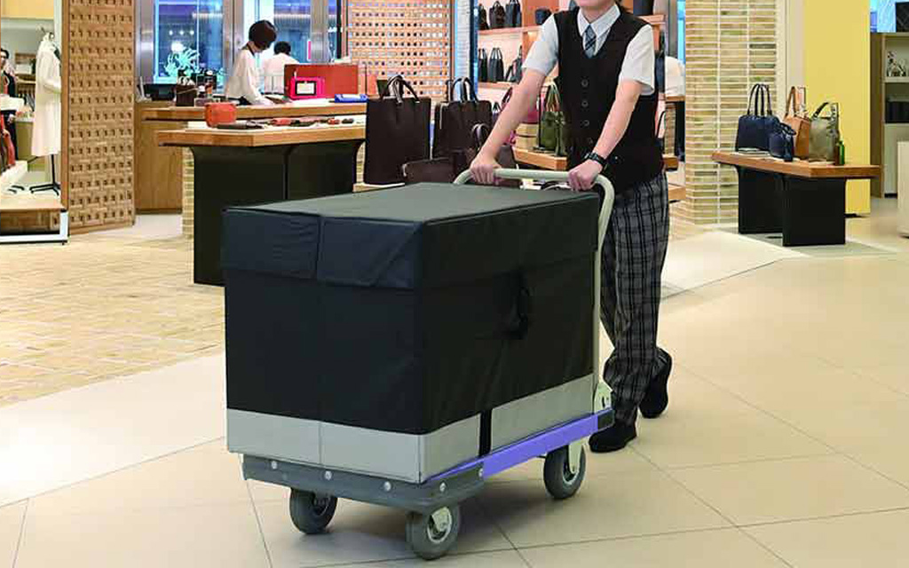 制服を着た人物が、黒い布で覆われた荷物を台車で押している。
