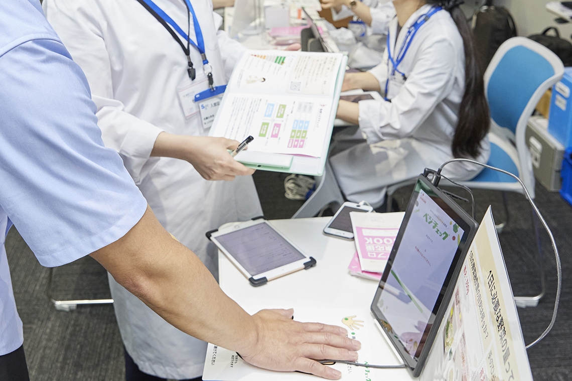 食生活改善を促す「野菜摂取の見える化イベント」を実施。測定機に手をのせて野菜摂取量を測定する様子。